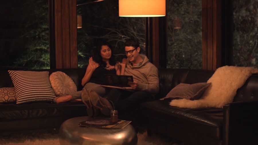 two people sit on a couch next to a dimly lit lamp.