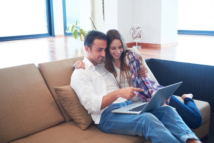 A man and woman sitting on a couch with a laptop.