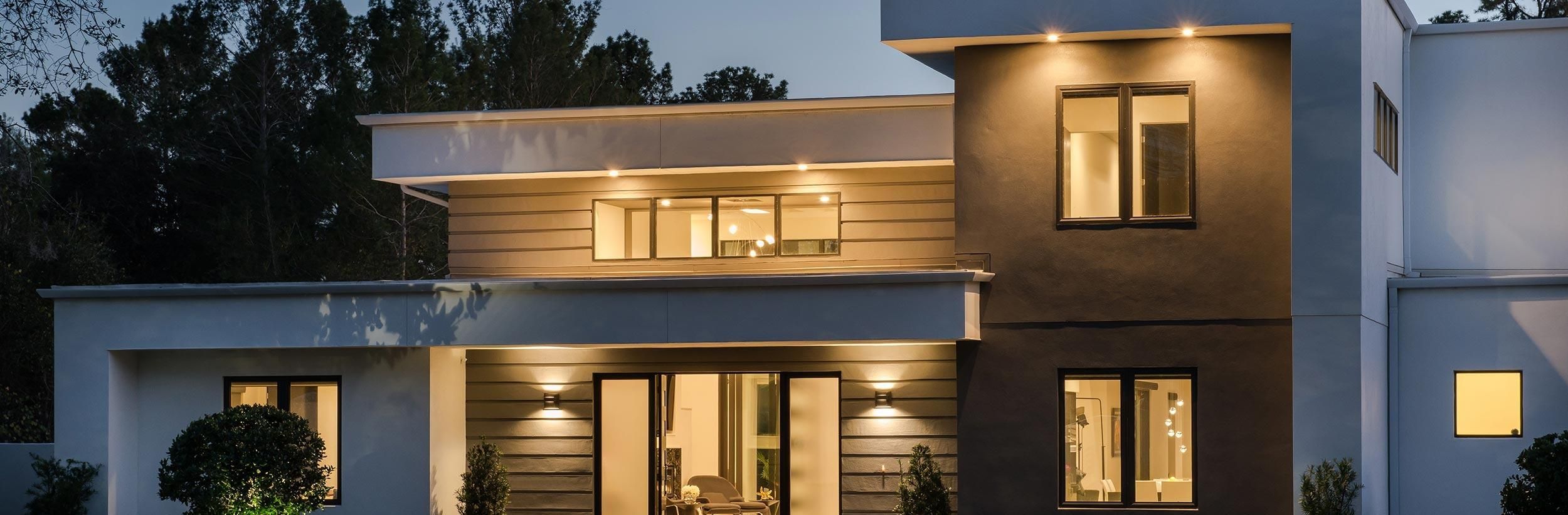 Modern home exterior illuminated with downlights showcasing architectural features and large windows.